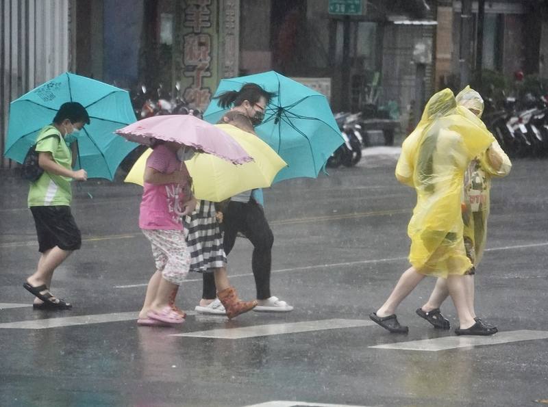 圖為高雄市苓雅區2日午後風雨轉強，街頭民眾穿著雨衣、撐傘在強風雨勢中前行