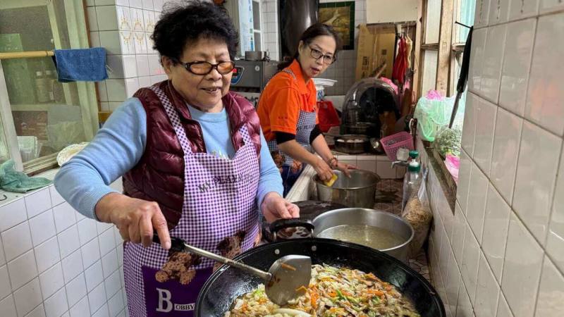 弘道南港社區照顧關懷據點7日提前舉辦圍爐餐，80歲阿嬤李甚（前左）在廚房忙進忙出，擔任辦桌總舖師，多名據點長輩當「水跤」，開席6桌請客，全是親手煮的手路菜。（弘道老人福利基金會提供）