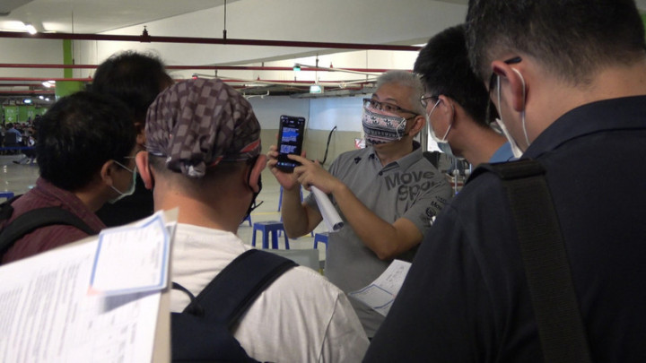 在慈濟印尼分會協助下，雅加達台灣工商聯誼會安排台商接種疫苗，圖為台商會前秘書長郭東義（持手機者）在22日向僑胞說明，應留意透過手機簡訊傳送的疫苗施打證明。