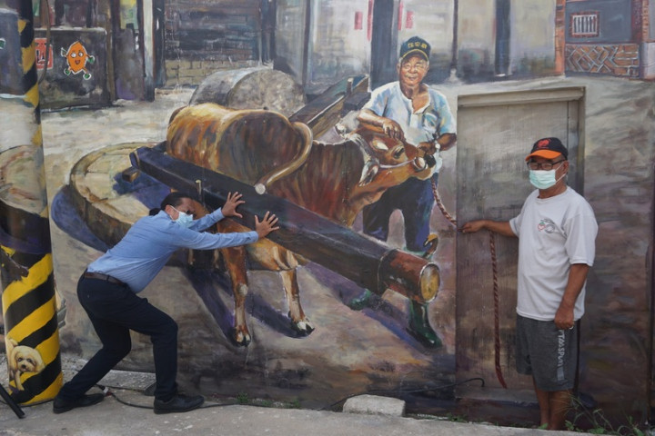 金門首屆駐縣藝術家鄒佳哲（左）重返舊地，為何厝社區彩繪壁畫，畫中甘藷石輪等何厝特色盡收眼底，鄒佳哲盼成為金門打卡景點，為何厝注入活力。