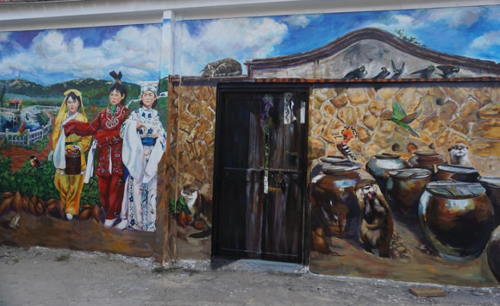 金門首屆駐縣藝術家鄒佳哲重返舊地，為何厝社區打造「番薯故事館」壁畫，在原本光禿禿的水泥牆面上彩繪出古老地瓜酒缸和歐亞水獺、戴勝等動物，栩栩如生；鄒佳哲也期許壁畫能成為金門六星級打卡新點。