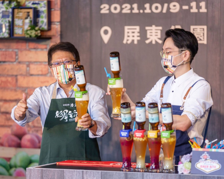 屏東縣政府首創「屏東縣微生物菌種資材中心」，經一年培訓，以澆灌光合菌在地水果結合啤酒頭，打造「初昇」、「佐光」2款精釀啤酒，縣長潘孟安（左）28日記者會中行銷。（屏東縣政府提供）