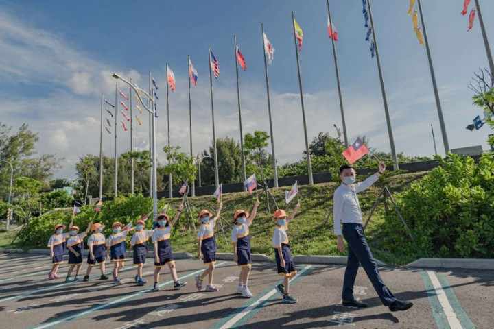 為感謝捐贈台灣疫苗的日本、美國、立陶宛、斯洛伐克、捷克、波蘭等6國，新竹漁港25日升起6盟友國旗，新竹市長林智堅（右1）也與國小學童一起舉起國旗合影。（新竹市政府提供）