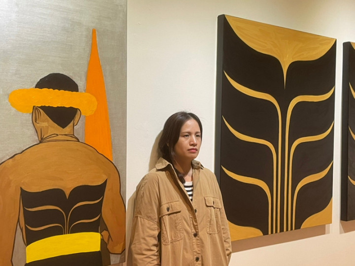 屏東美術館「我們與未來的距離－安力．給怒、宜德思．盧信雙個展」26日登場，展期至111年2月27日，展出2人近50幅作品。圖為宜德思．盧信和她的作品。（屏東縣政府文化處提供）