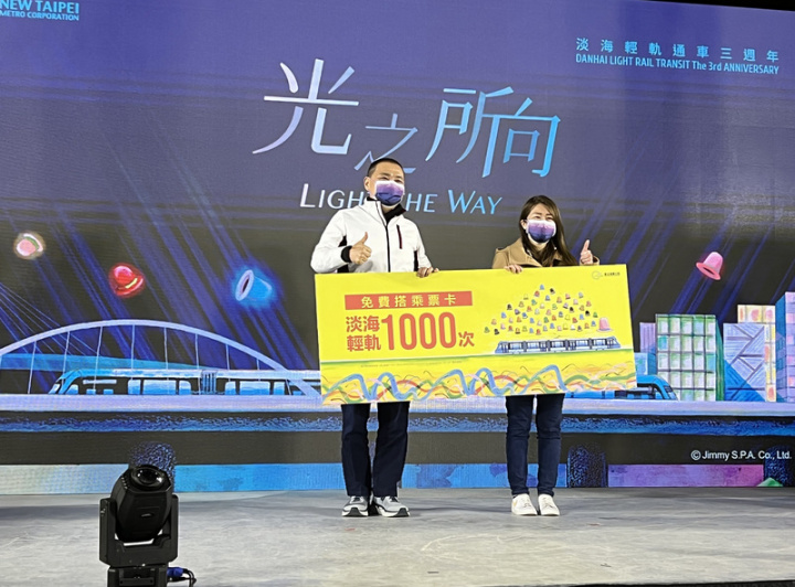 新北淡海輕軌3週年光影列車秀15日晚間登場，活動並邀來輕軌第1000萬名幸運兒乘客林小姐（右），由市長侯友宜（左）送上象徵可免費搭乘1000趟次的看板。林小姐笑說，她搬到淡水2年，沒想到會成為第1000萬名乘客。
