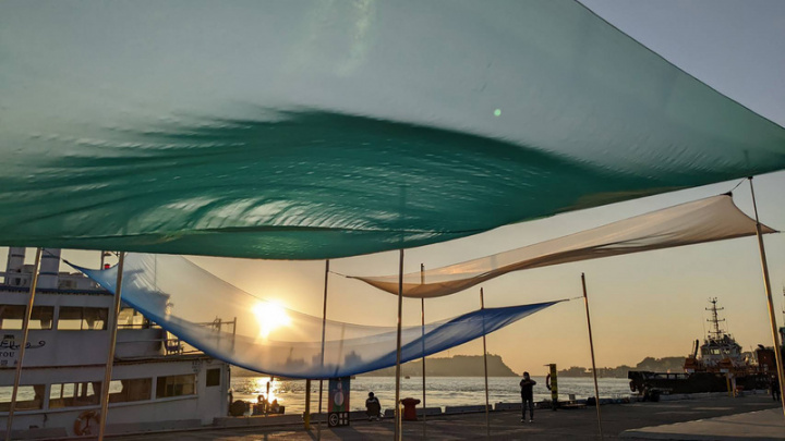 台灣港務公司攜手藝術家們在高雄港區推動公共藝術整體規劃，打造多樣公共藝術作品，其中限期展出的「波光」透過布幔隨風上下浮動，營造浪漫美感。