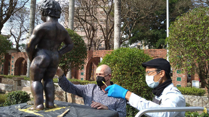 嘉義市政府委託古物修復專家泰納沃克（左）與張志鵬（右）合作，進行嘉義公園尿尿小童銅像修復工作，耗時1個多月細心除漆，已回復應有的顏色，五官也變得清晰，目前正做細部處理。