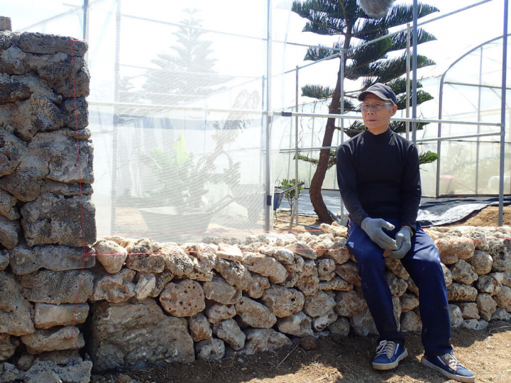 接觸澎湖傳統堆砌咾咕石牆技藝、居住在澎湖縣湖西鄉湖東村的許仁雄，11日在湖東防風教室親手示範一段利用咾咕石手作疊砌菜宅和步道等工法技藝，並直接坐上疊砌好的石牆休憩。（台灣千里步道協會提供）