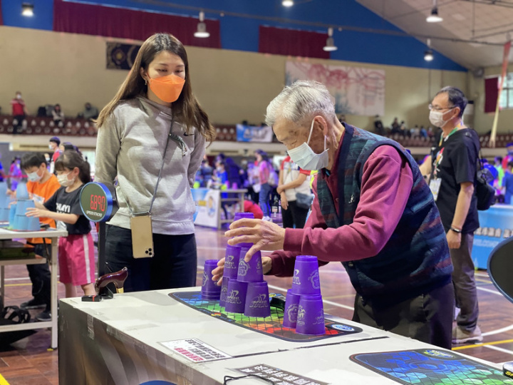 111年全國競技疊杯錦標賽12日在新北市新莊區恆毅中學開幕，本屆最高齡參賽者為來自坪林水柳腳公共托老中心的94歲長者林有德（前右）。（主辦單位提供）