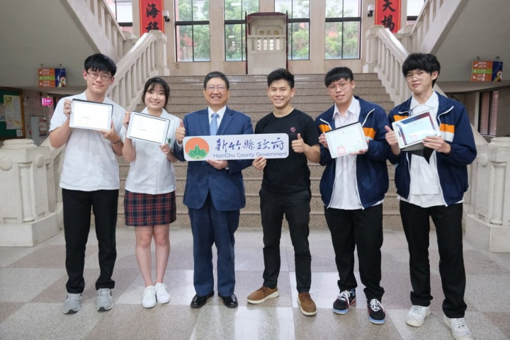 新竹縣政府21日表示，與來自矽谷的新創公司圖靈鏈合作，共同發行不可篡改的「區塊鏈數位證書」，湖口及六家高中率先推行，2022年共476畢業生將領取，接軌國際。圖為縣立湖口與六家高中學生秀出「區塊鏈數位證書」，縣長楊文科（左3）見證。（新竹縣政府提供）