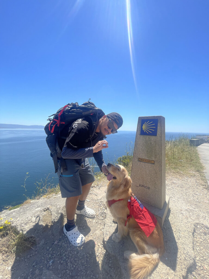 來自台灣的黃金獵犬Money和主人Burger Han（臉書帳號），在西班牙加利西亞地區菲尼斯特雷（Finisterre）海角旁，佇立的朝聖之路「0公里」石碑前合影。菲尼斯特雷位在大西洋海岸線上，過去被認為是歐陸的終點，因此被稱為「世界的盡頭」。有些朝聖者在抵達終點站後，會繼續上路走到此地。（Burger Han提供）