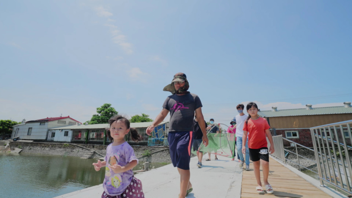 好蝦冏男社社長 李富正與女兒們一起在魚塭旁，帶領遊客體驗捕蝦。