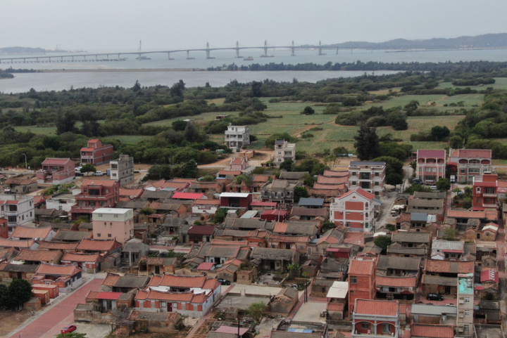 金門大橋（後）西起烈嶼后頭地區、東迄於金寧鄉慈湖地區，路線全長約5.4公里，其中約4.77公里位於海上，日前已辦理大橋通車前履勘，相關改善事項可於28日完成，預計30日開放通車。圖前為111年10月19日金門縣金寧鄉南山聚落，古厝成群。