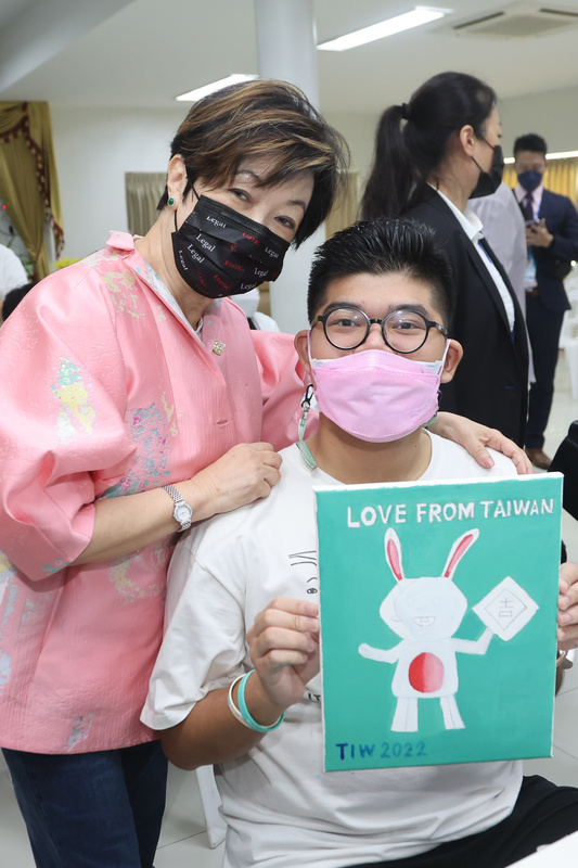 台灣APEC領袖代表張忠謀夫人張淑芬（左）19日參 訪泰國自閉症基金會，與孩子們分享創作經驗，一名 孩童在畫作上寫下「LOVE FROM TAIWAN」，兩人 一同合影留念。