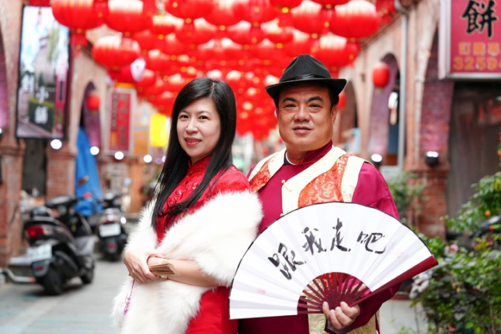 金門縣金城鎮別具特色的模範街最近掛上成排大紅燈籠及部分兔年燈飾，應景搭配即將到來的農曆春節，鎮長李誠智（右）與太太吳品珊（左）也穿起古裝邀請民眾到訪。（金城鎮公所提供）