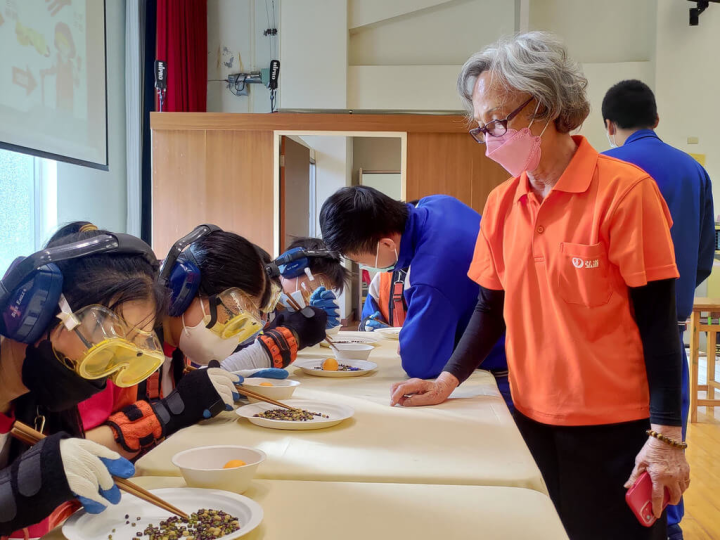 弘道老人福利基金會在台中市太平國中舉辦「體驗老世界」活動，由8旬長者謝秀環（前右）帶領國中生穿上模擬老化裝備，親身體驗高齡者視茫、重聽、駝背、行動不便等生理退化情況。（弘道老人福利基金會提供）