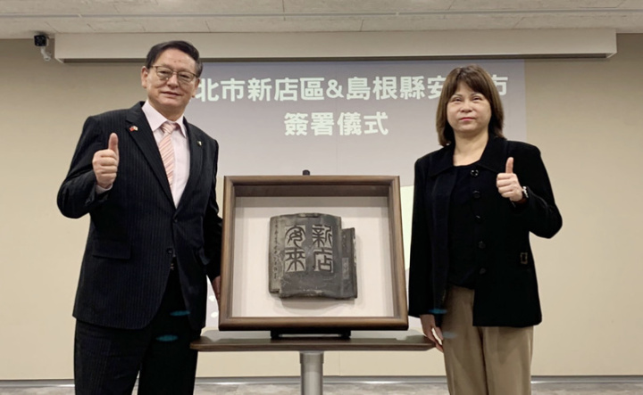 新北市新店區長陳怡君（右）與日本島根縣安來市長田中武夫（左）7日簽署「友好交流都市備忘錄」，陳怡君致贈由知名毫芒藝術家陳逢顯以有80年歷史的日本黑瓦創作作品，並雕刻「新店安來」字樣，象徵雙方友誼。