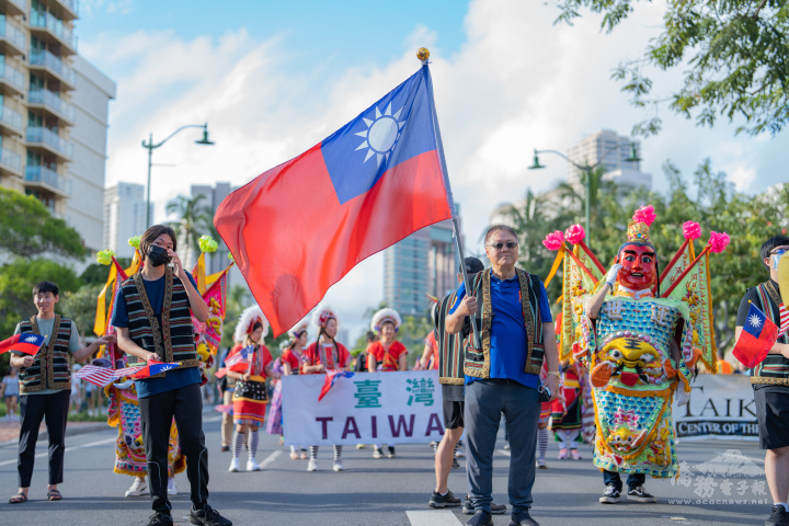 僑胞身穿阿美族服飾，手舉臺灣字牌與國旗，邁步跟著閃亮三太子打遊行頭陣。（林原民提供）