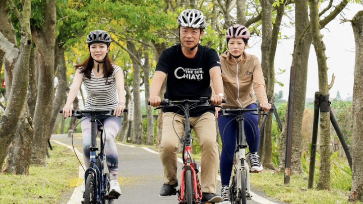 嘉義縣朴子溪自行車道兩旁的阿勃勒花即將盛開，嘉義縣長翁章梁（中）13日前往拍攝宣傳影片，歡迎民眾來「嘉」騎車，享受田園風光。