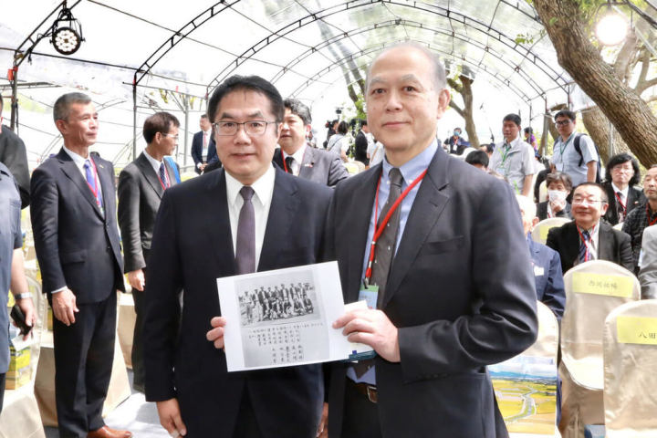 台南市長黃偉哲（前左）8日出席八田與一追思紀念會，贈送祖父黃濱田在嘉南大圳管理站任職的老照片給八田與一的長孫八田修一（前右）。（台南市政府提供）