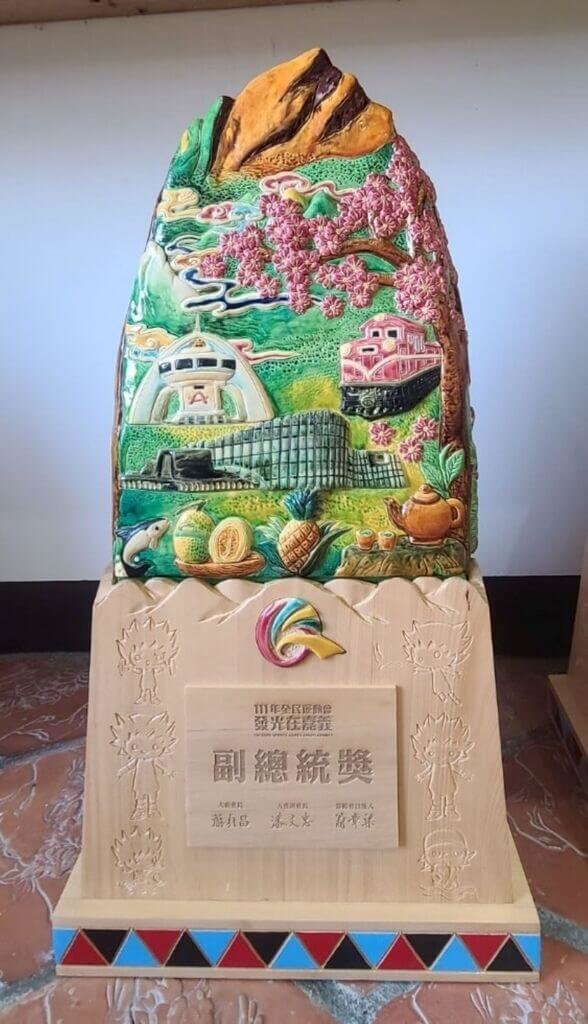工藝家謝東哲為111年全民運動會創作的交趾陶獎座，雕塑出阿里山日出、小火車、櫻花、茶園、北回歸線、故宮南院等嘉義在地景物。（謝東哲提供）