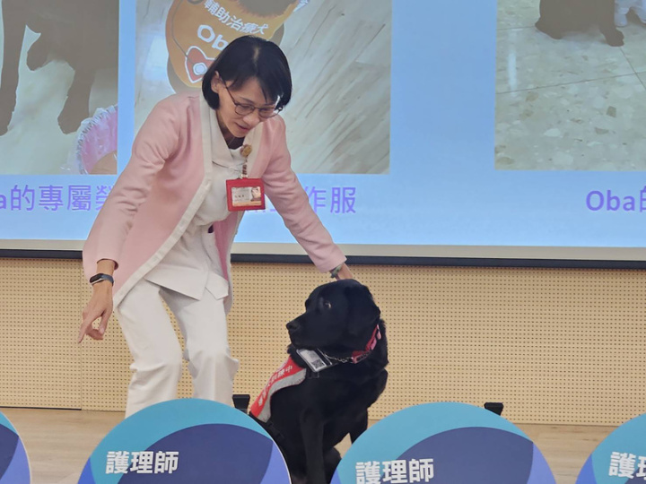 台北榮民總醫院大德病房，有一隻黑毛狗的「歐巴」Oba，在經過3個月訓練，由安寧病房護理師劉曉菁（圖）正式成為輔助治療犬合格寄養家庭，變成Oba「大媽」，Oba從108年2月開始任職至今，甚至有專屬榮總職員證和工作證。
