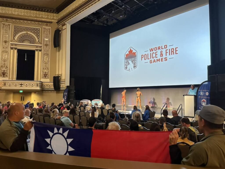 第20屆世界警察消防運動會在加拿大舉行，警政署30日公布首日3金4銀佳績，獲獎選手上台領獎，代表團成員也在場邊舉國旗吶喊加油。（警政署提供）