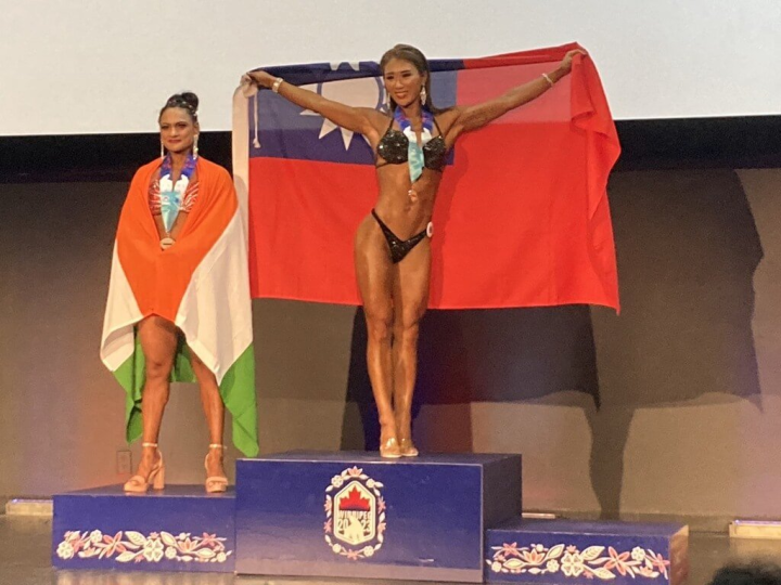 第20屆世界警察消防運動會在加拿大舉行，警政署30日公布首日賽事成果，台灣代表團勇奪3金4銀佳績。圖為台北市警察局王令樺（中）在女子健美健體及比基尼項目摘下雙金，披掛國旗領獎。（警政署提供）