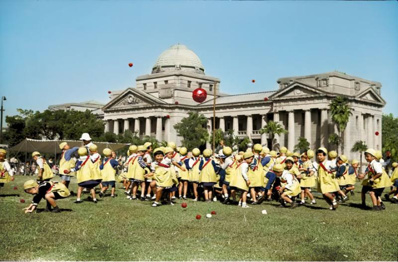 幼稚園的運動會，背景為今二二八和平紀念公園內的台灣博物館。王佐榮還考證出孩童玩的遊戲是源自西班牙語地區的「Piñata」，遊戲規則要用沙包把懸吊的紙糊彩球擊破；依據日本的習俗，分成的兩隊當然是以紅白兩色區分。（出自《彩繪鄧南光》）