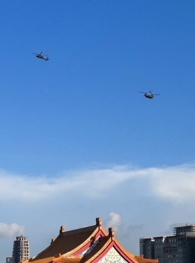 國慶將至，國軍26日進行半兵力預演，其中1架UH-60M黑鷹直升機（左）與游懸掛巨幅國旗的CH-47SD契努克運兵直升機（右）通過總統府上空。