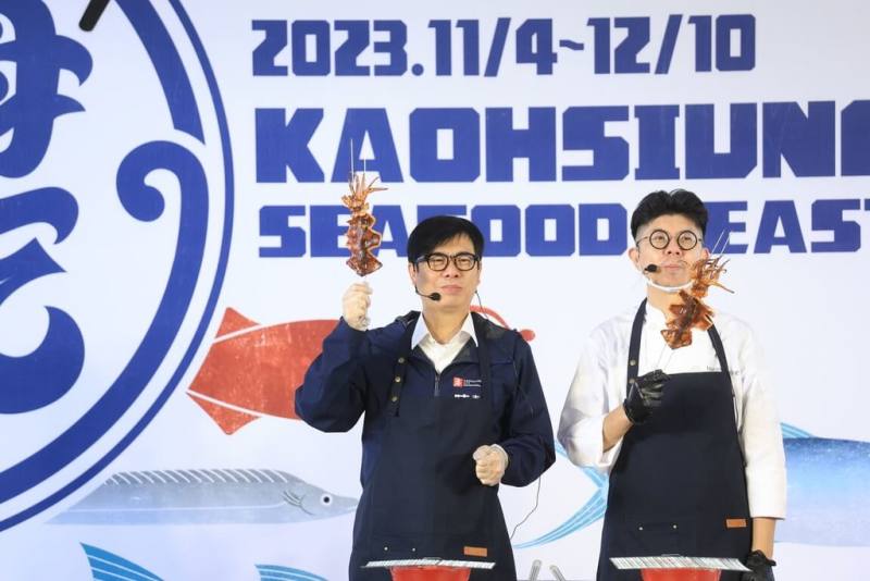 高雄市長陳其邁（左）25日出席「2023大海開吃」系列活動記者會，與高雄Le Bon Marché好市集手作料理主廚黃穎（右）一同現烤魷魚，歡迎民眾揪團觀光吃海鮮。（高雄市政府提供）