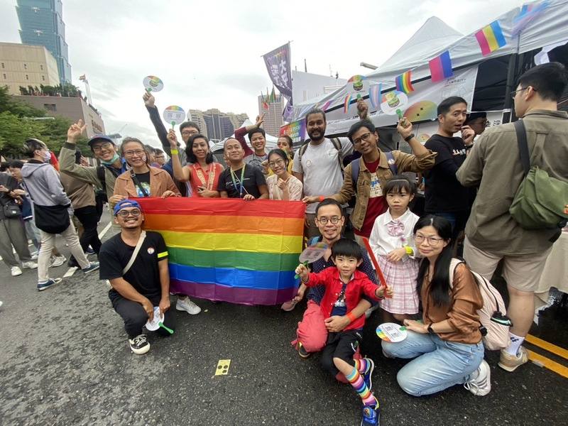 台灣同志遊行今年邁入第21屆，不少民眾在中午時就湧入北市府前廣場，等著參加午後遊行。台灣海外援助發展聯盟秘書長李尚林（抱紅衣男孩者）特別帶著10名東南亞資深NGO工作者來台參加。