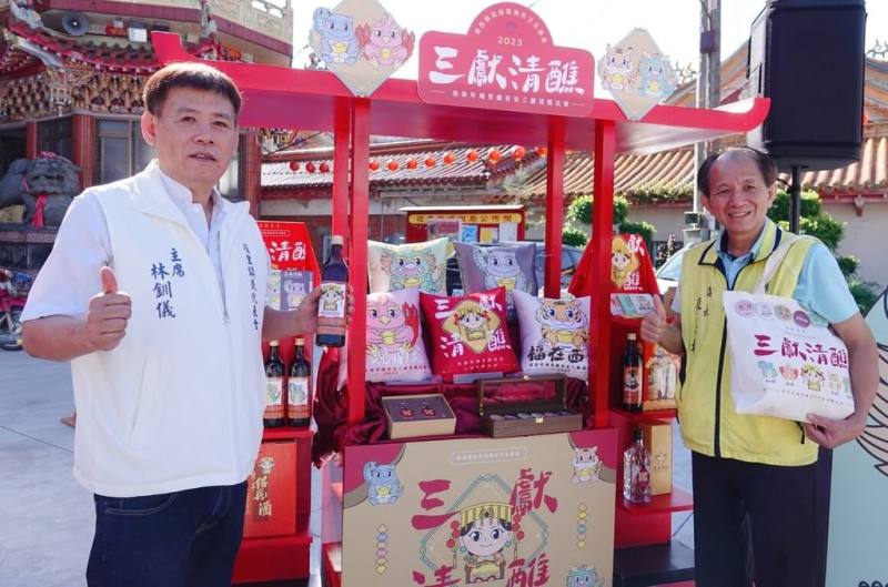 南投縣埔里鎮祈安三獻清醮法會12月登場，主辦單位結合文創推出上衣、胸章、皮革平安符、抱枕、明信片、提袋、杯墊等紀念品，埔里鎮長廖志城（右）與埔里鎮民代表會主席林釧儀（左）8日向外界宣傳。（埔里鎮公所提供）