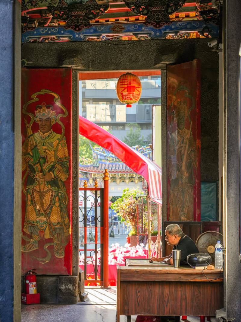 台北市老房子影像徵件攝影展26日開展，其中首獎得主沈家祥所拍攝的市定古蹟艋舺清水巖，以廟宇神祇視角，向外凝視廟公、門神及廟埕喜宴流水席，呈現歷史與現代交融的畫面。（台北市文化局提供）