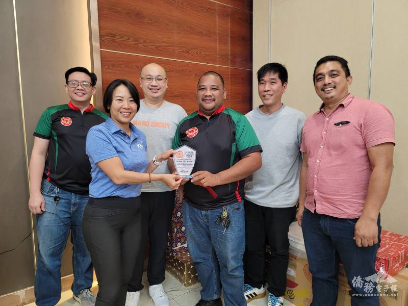 楊瑜玉(左)頒贈2023年傑出小隊長獎盃及紅包獎金予柯文明(右)，並由王英群(後排右2)、李益群(後排左2)、柯順敏(後排左1)、吳肇峰(後排右1)等人見證