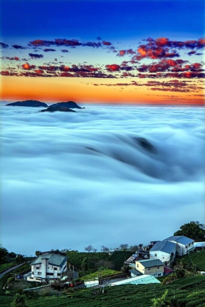 嘉義縣竹崎鄉中和村石棹民宿區雲層變化吸睛，攝影師蘇再明18日上午更拍下橘紅色雲朵、霞光、白色雲瀑、建築與茶園相互交織而成的美麗畫面。（蘇再明提供）