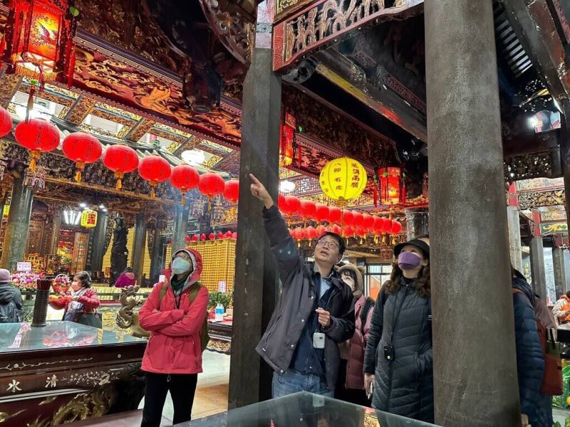 春節連假期間，與新北捷運合作的淡水在地走讀團體「旅學堂」帶路人吳峻毅（舉手者）帶領民眾搭乘淡海輕軌，走訪淡水區清水祖師廟等廟宇，近距離了解傳統彩繪藝師莊武男藝術成果。（旅學堂提供）