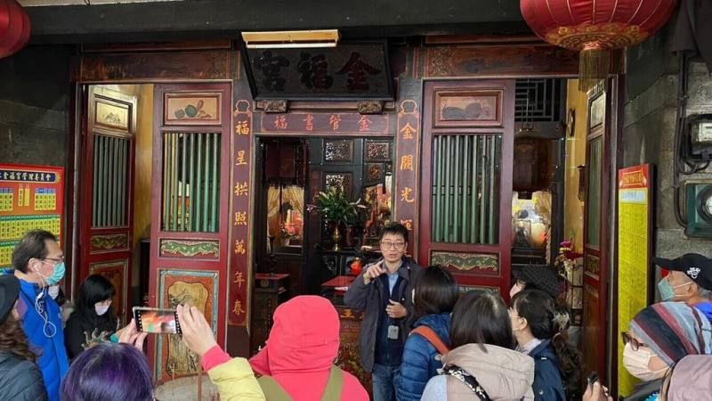 新北市淡水在地走讀團體「旅學堂」帶路人吳峻毅（後中）帶領民眾一起走進淡水金福宮，介紹傳統彩繪藝師莊武男在廟廊前彩繪作品。（旅學堂提供）