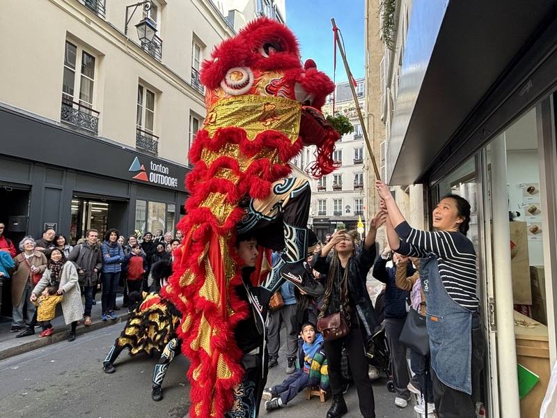 17日巴黎市台灣車輪餅店Ciao Roue前門庭若市。法國人古思萬帶領的「法國民社館忠義堂」正在表演舞獅的「採青」橋段，採青如今衍生之意取生菜和「生財」的諧音，為商家帶來好彩頭。