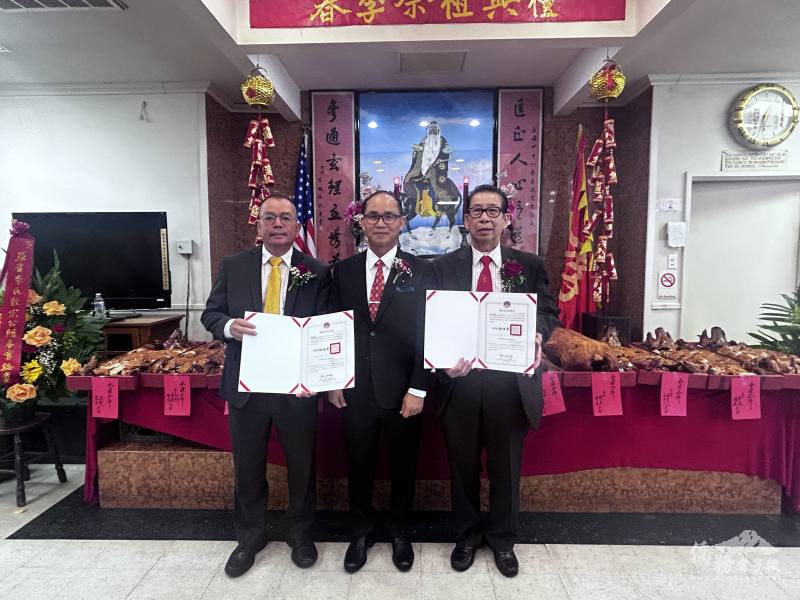 張正育代僑委會委員長徐佳青致頒賀狀予續任主席李焯漢(右)、副主席李錦生(左)