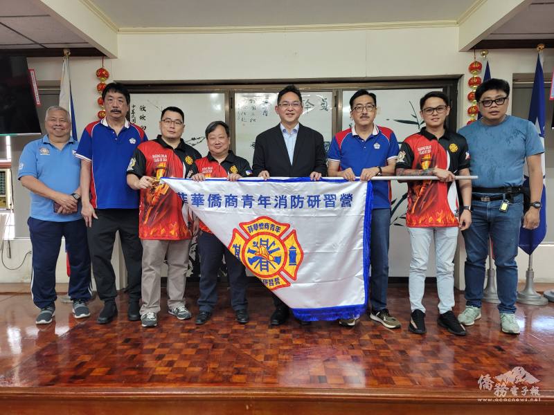 莊博智（右4）、吳治平（右3）將菲華青年消防研習營旗幟交予團長蔡彼得（左4），副團長蔡立夫（左3）、陳僑順（右2）