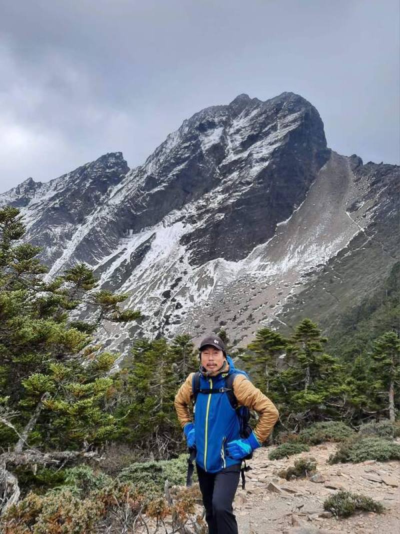 畫家王德合（圖）說，他將個人的山林體驗，用寫實繪畫技巧、變動的色彩，或以繪畫造形遊走在客觀寫實山景與主觀變動感受之間，傳達及分享心中山林幻化之美。王德合後方為玉山主峰。（王德合提供）