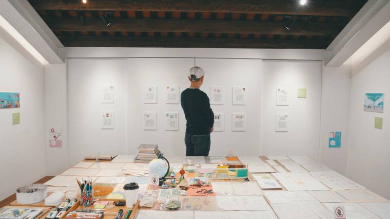 繪本作家湯姆牛首辦個展「湯姆牛．幾分熟？」即日起在台北展出，展區中央的大型工作桌是直接從湯姆牛家中挪移到展場，上面鋪陳各種關於他的生活、靈感、手稿、腳本以及孩子們送的禮物等。（小天下出版提供）