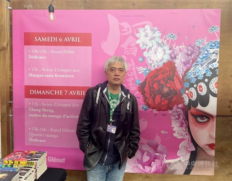 Taiwanese mangaka Chang Sheng poses in front of an event poster which depicts the cover art of the first volume of his superheroine comic "Yan" at Foire du Livre de Bruxelles (Brussels Book Fair). The event post also detailed Chang Sheng's appearance at t