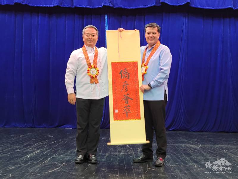 周民淦（左）代表僑務委員會委員長徐佳青贈送「僑彥薈萃」賀軸予菲華青年服務團總團部，並由理事長謝銘洲（右）代表接受