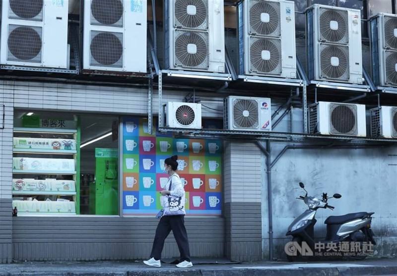 A woman walks past by a building fitted with several air conditioners in New Taipei.