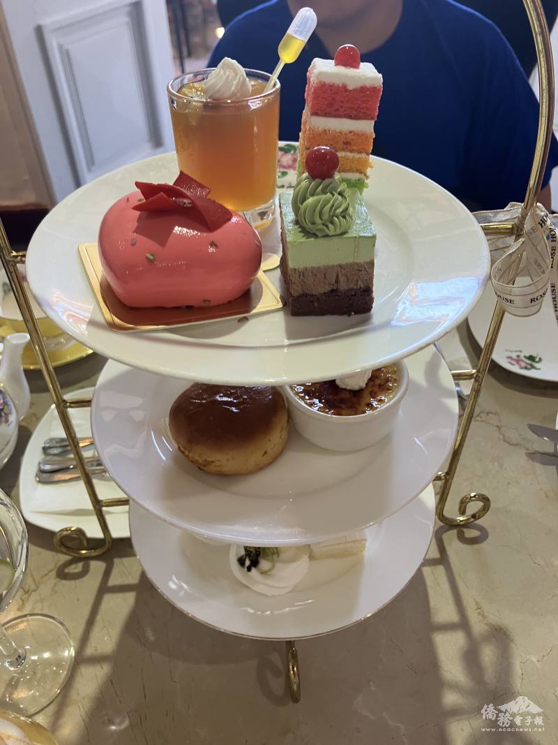 A three-tiered serving tray showcasing (from top to bottom): small square sandwiches and caviar meringue; crème brûlée and scones with rose jam; an assorted selection of sweet desserts.