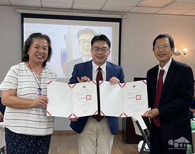 周啟宇(中)代表僑委會頒贈賀狀予新任會長方志峯(右)及滿任會長鍾世芬(左)感謝狀