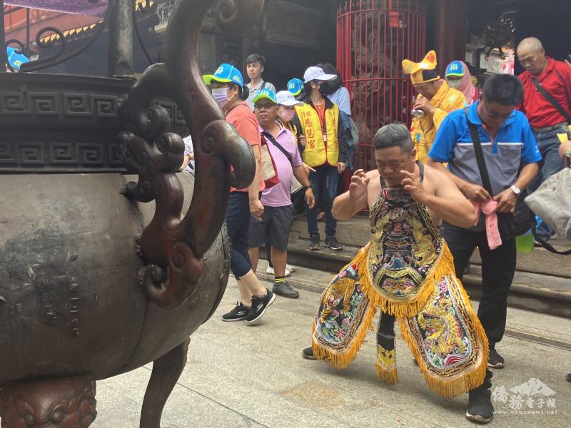 A dancer, dressed in a special yellow dragon outfit, performs rituals in front of a large incense bowls.