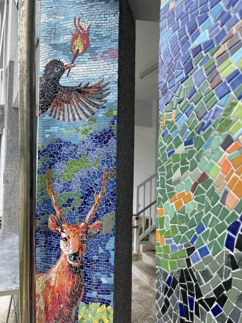 嘉義縣阿里山鄉達邦國小鄒族神話藝術牆近日完工，藝術牆旁的柱子描述「天神取火」傳說，有紅嘴黑鵯銜著火把飛躍及水鹿凝視前方的畫面。（歐志成提供）